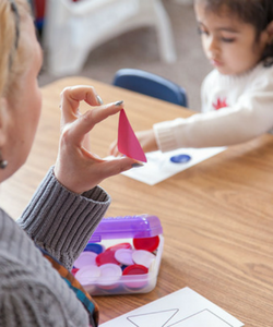 A teacher holds up a shape for a preschool student