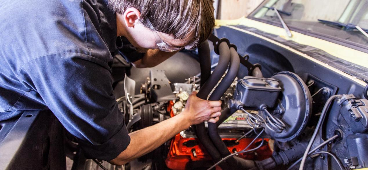 Image of student working on hoses under a truck hood