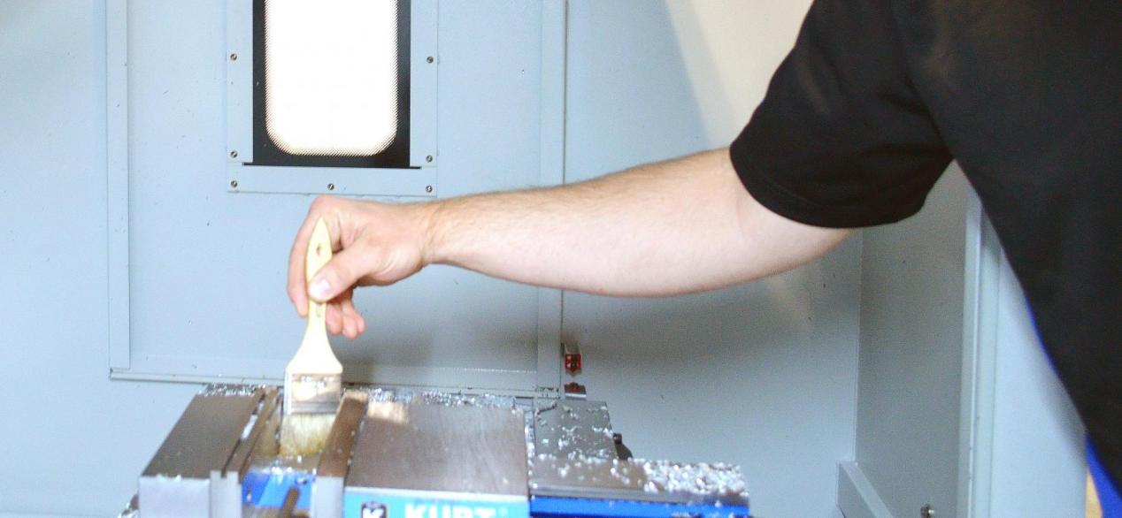 Student brushing chips from a milled part inside a CNC machine