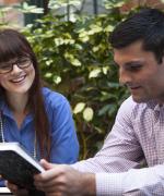 Image of a young man looking at a book while a lady looks on